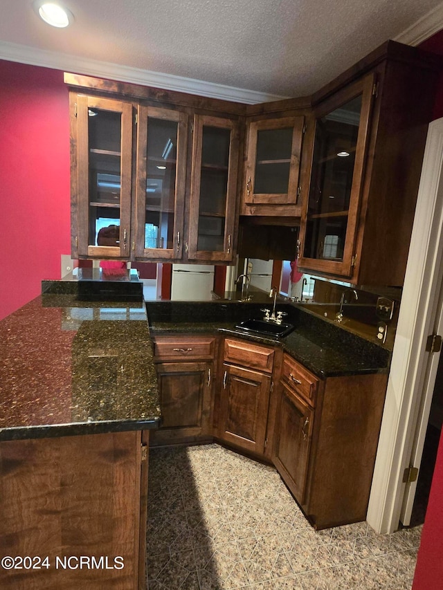 kitchen featuring sink, dark brown cabinets, a textured ceiling, dark stone countertops, and crown molding