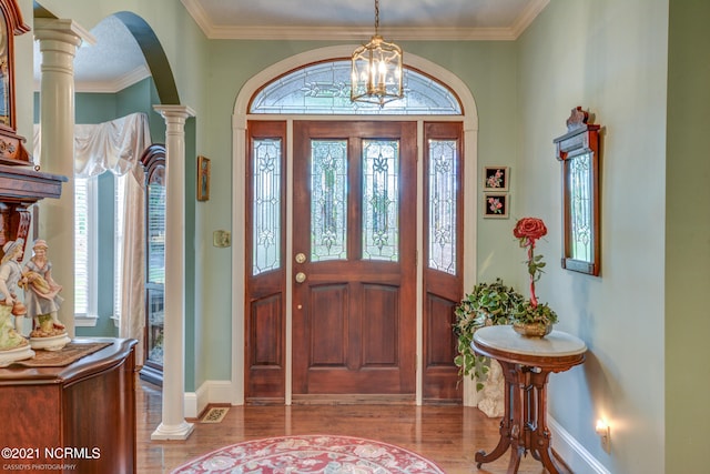 foyer with a notable chandelier, ornamental molding, hardwood / wood-style flooring, and decorative columns