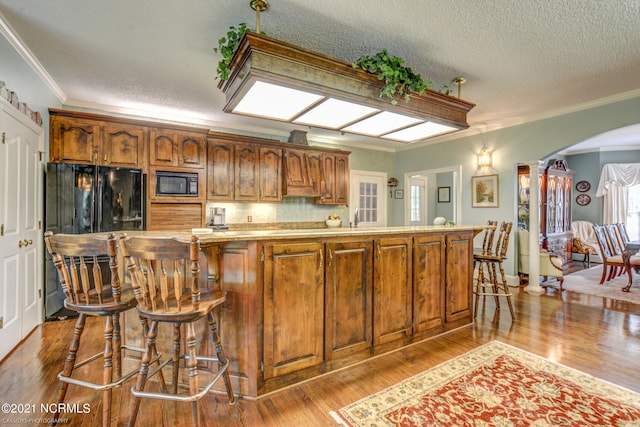 kitchen featuring a textured ceiling, light hardwood / wood-style flooring, crown molding, and black appliances