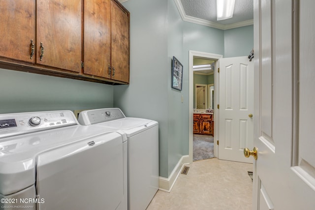 washroom with a textured ceiling, ornamental molding, washing machine and clothes dryer, and cabinets