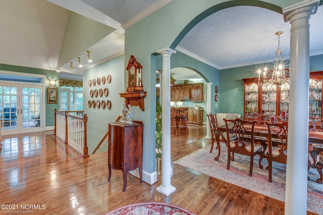 dining room with ornate columns, light wood-type flooring, lofted ceiling, ornamental molding, and a notable chandelier