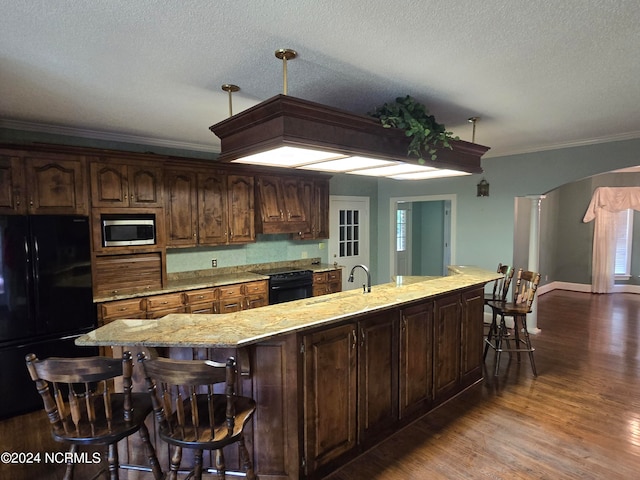 kitchen featuring dark brown cabinetry, black appliances, a spacious island, crown molding, and dark hardwood / wood-style flooring