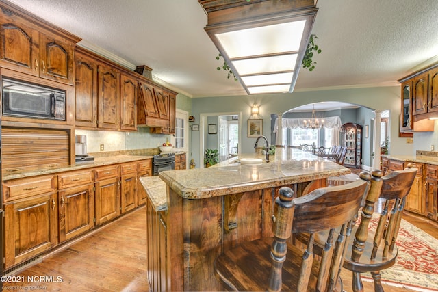 kitchen with an island with sink, a breakfast bar, black appliances, crown molding, and sink