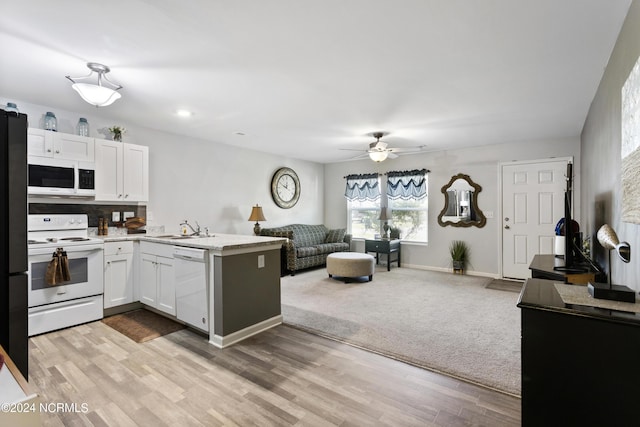 kitchen featuring white appliances, open floor plan, a peninsula, light countertops, and a sink