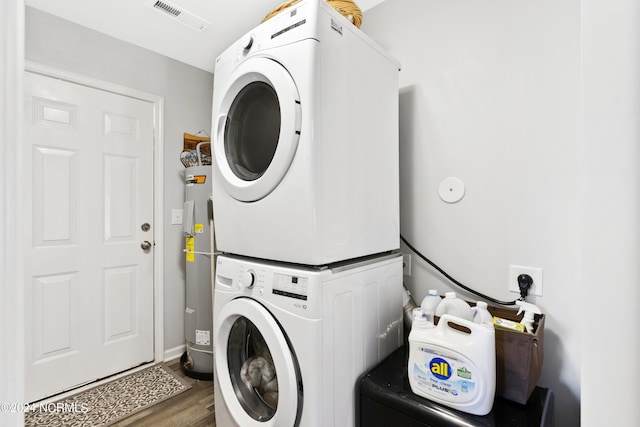 laundry room featuring laundry area, stacked washer and dryer, visible vents, wood finished floors, and electric water heater