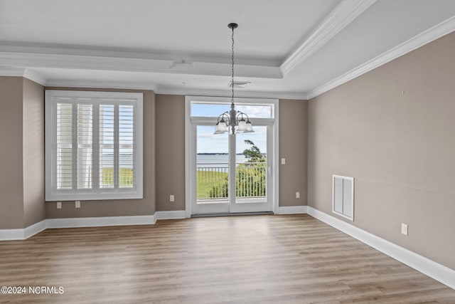 unfurnished dining area featuring a raised ceiling, ornamental molding, light wood-type flooring, and a chandelier