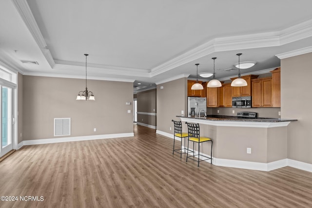 kitchen with hardwood / wood-style floors, ornamental molding, stainless steel appliances, hanging light fixtures, and a tray ceiling