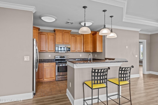 kitchen featuring wood-type flooring, appliances with stainless steel finishes, a kitchen bar, kitchen peninsula, and ornamental molding