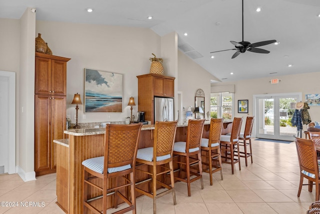 kitchen with light stone counters, stainless steel refrigerator, high vaulted ceiling, and ceiling fan