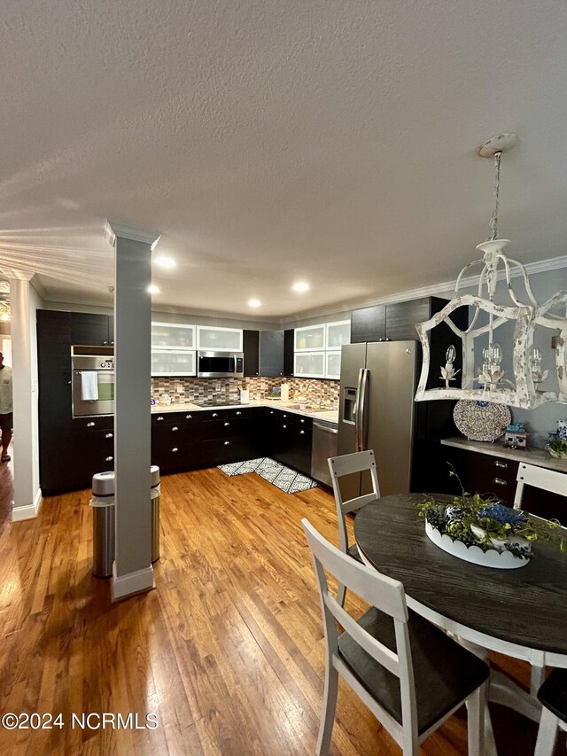 kitchen with light hardwood / wood-style flooring, decorative columns, stainless steel appliances, ornamental molding, and decorative backsplash