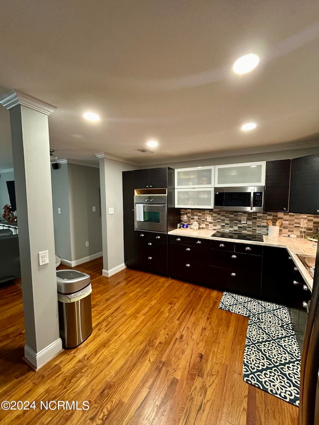 kitchen featuring decorative columns, light hardwood / wood-style floors, crown molding, stainless steel appliances, and decorative backsplash