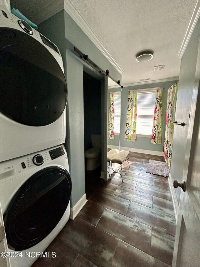 washroom with a barn door, stacked washer and clothes dryer, crown molding, and a textured ceiling