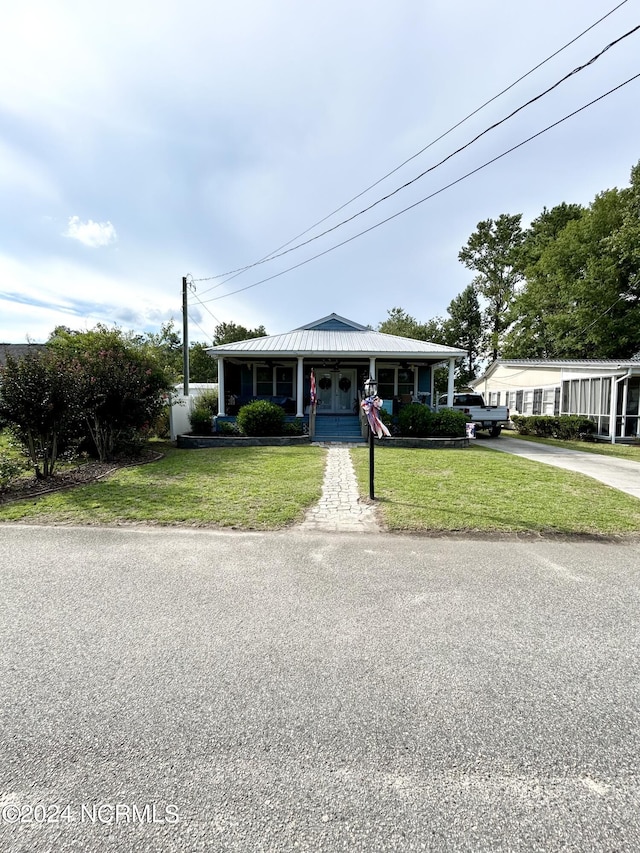 view of front facade with a porch, a front yard, and metal roof