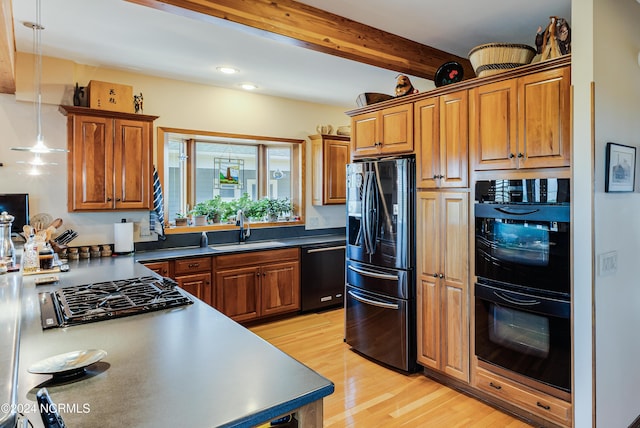 kitchen with decorative light fixtures, beamed ceiling, sink, black appliances, and light hardwood / wood-style flooring