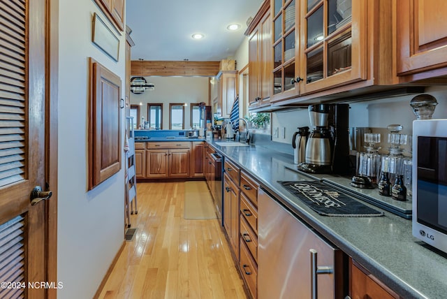 kitchen with stainless steel appliances, brown cabinetry, glass insert cabinets, and light wood-style floors