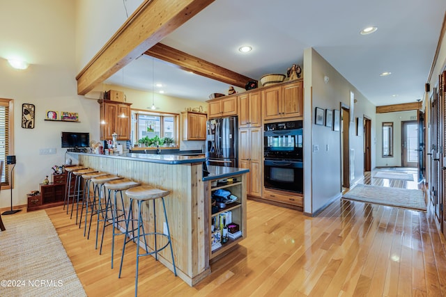 kitchen with kitchen peninsula, beamed ceiling, a breakfast bar area, black appliances, and light wood-type flooring