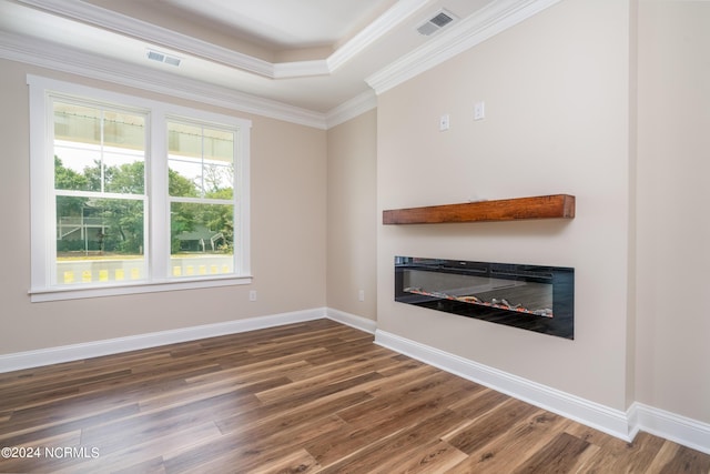 unfurnished living room with ornamental molding, a glass covered fireplace, visible vents, and wood finished floors