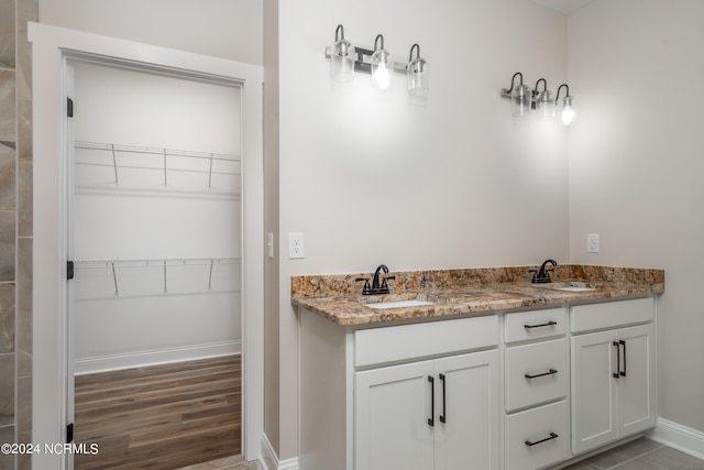 bathroom featuring baseboards, a walk in closet, a sink, and wood finished floors