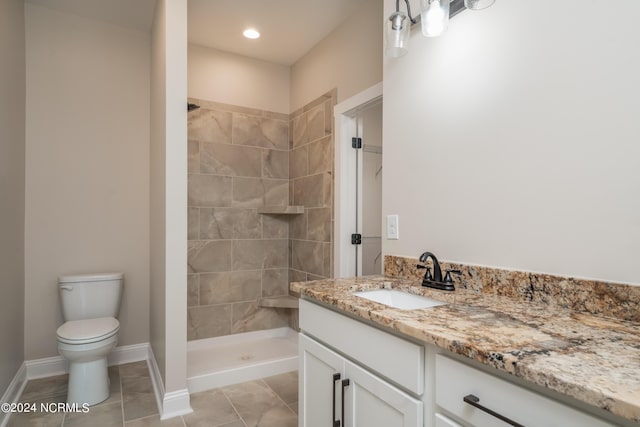 bathroom featuring baseboards, tiled shower, toilet, tile patterned flooring, and vanity