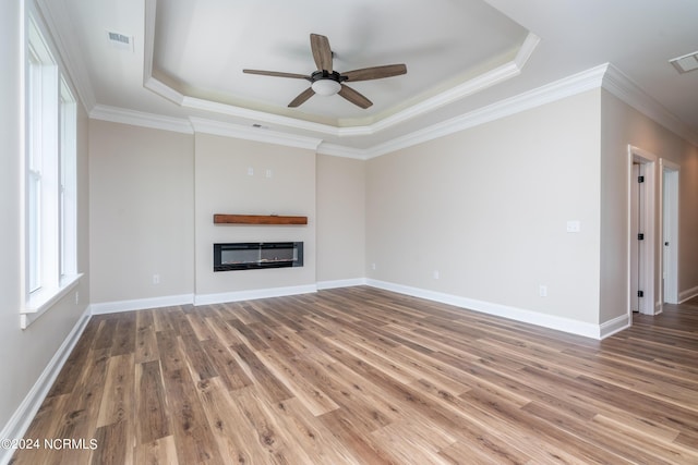 unfurnished living room with a tray ceiling, a glass covered fireplace, visible vents, and wood finished floors