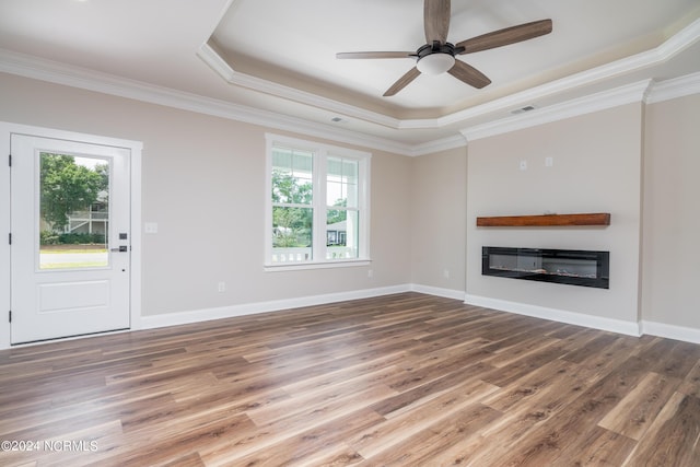 unfurnished living room featuring wood finished floors, a tray ceiling, a glass covered fireplace, and a wealth of natural light