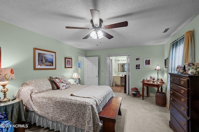 bedroom with a textured ceiling, connected bathroom, ceiling fan, and light colored carpet