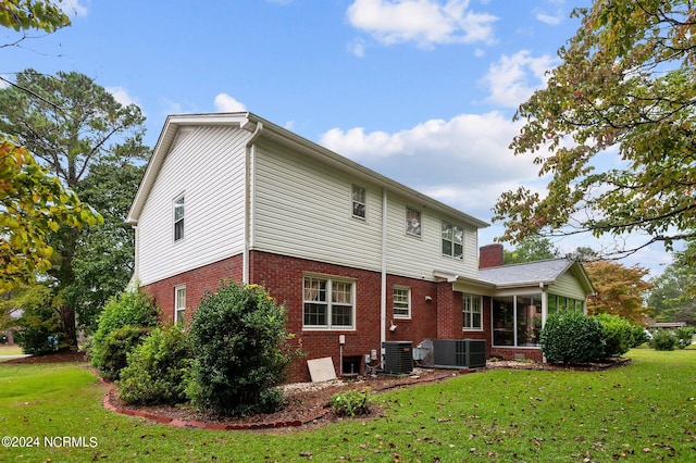 rear view of house featuring central AC unit, a sunroom, and a yard