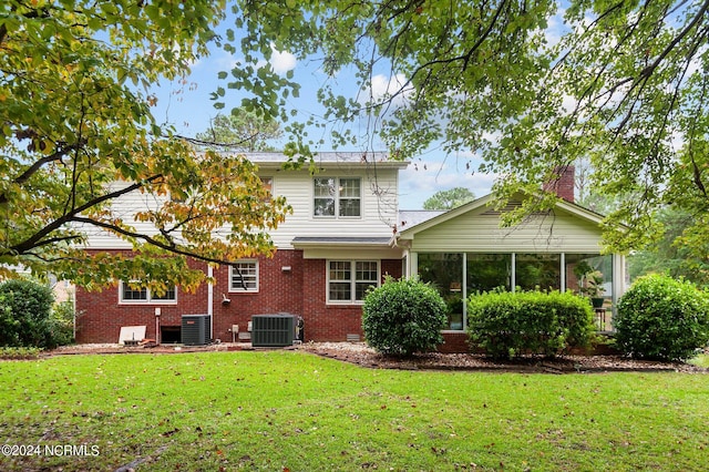 rear view of house with a lawn, a sunroom, and central AC unit