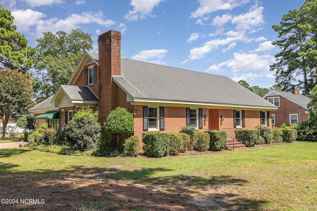 view of front of property with brick siding, a chimney, a front lawn, and roof with shingles