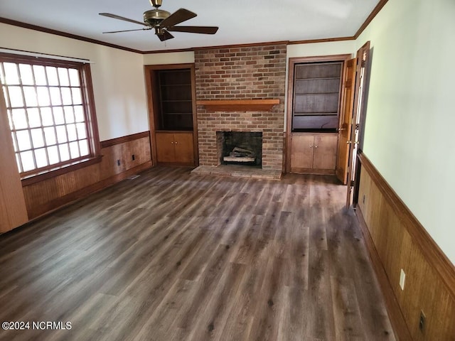 unfurnished living room featuring a brick fireplace, wooden walls, ceiling fan, dark wood-type flooring, and crown molding