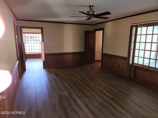 empty room featuring ceiling fan, ornamental molding, wooden walls, and dark wood-type flooring