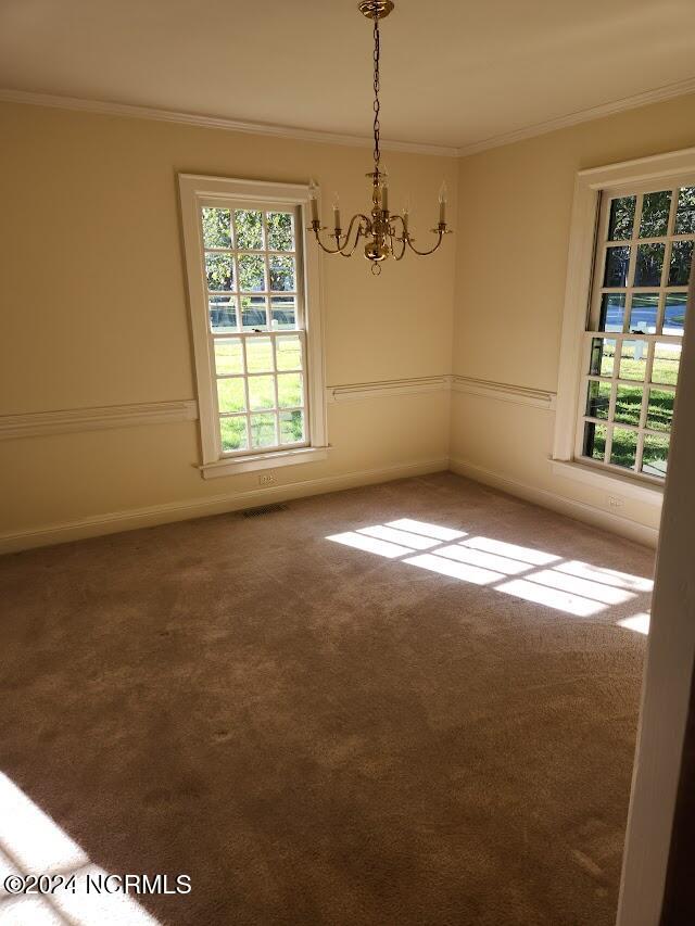 carpeted empty room with a notable chandelier and ornamental molding