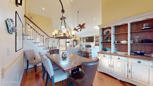 dining area featuring light wood-style flooring, an inviting chandelier, stairs, a fireplace, and high vaulted ceiling