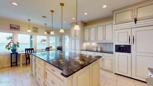 kitchen featuring dark stone counters, cream cabinetry, backsplash, a center island, and hanging light fixtures