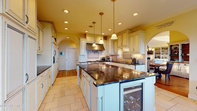 kitchen with hanging light fixtures, a center island, light wood-type flooring, dark stone counters, and beverage cooler