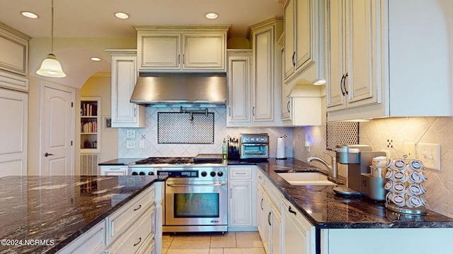 kitchen with dark stone countertops, backsplash, decorative light fixtures, and stainless steel stove