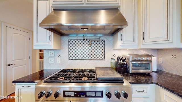 kitchen featuring stainless steel range oven, dark stone counters, wall chimney range hood, and white cabinets