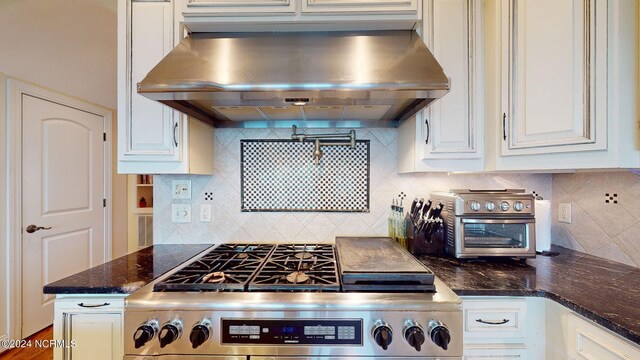 kitchen with dark stone counters, white cabinets, decorative backsplash, high end stove, and wall chimney range hood