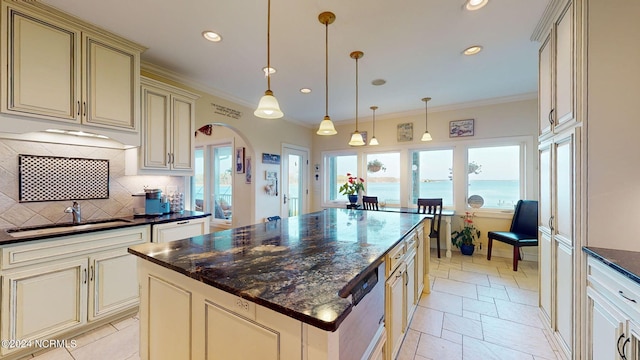 kitchen with dark stone countertops, pendant lighting, cream cabinets, and a center island