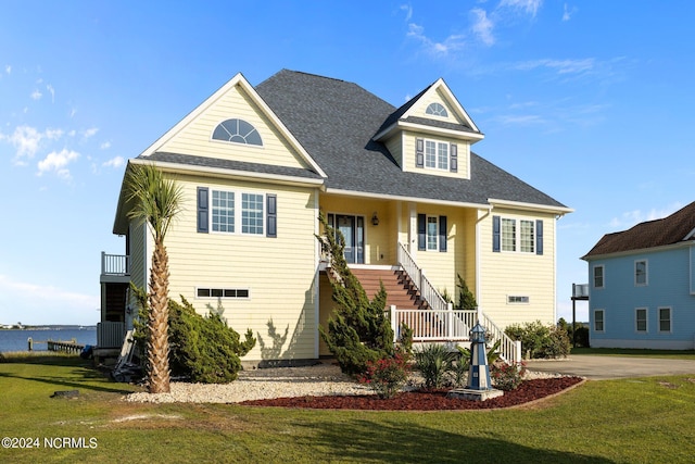 coastal inspired home with a front yard, roof with shingles, a water view, and stairway