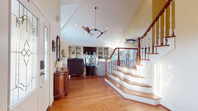 foyer entrance with high vaulted ceiling, light wood-style flooring, stairway, and a notable chandelier