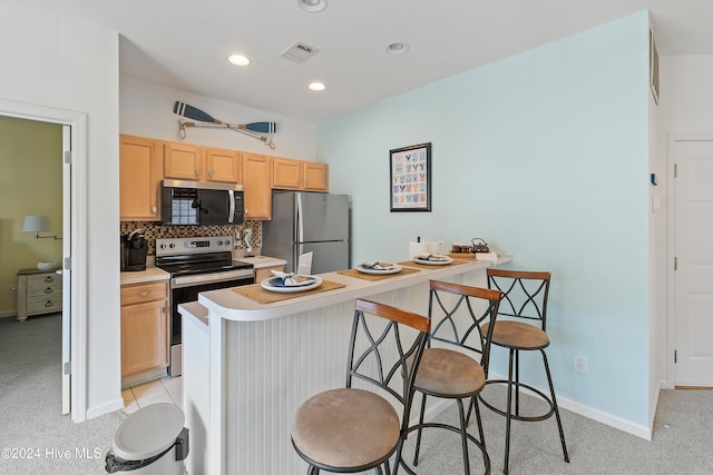 kitchen with a kitchen bar, appliances with stainless steel finishes, backsplash, light colored carpet, and light brown cabinets