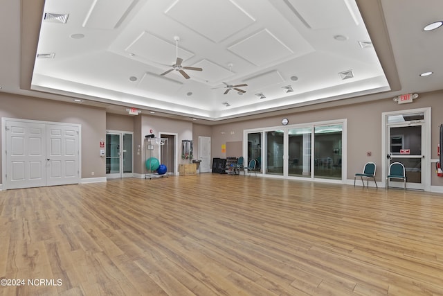 workout area with a raised ceiling, ceiling fan, and light wood-type flooring