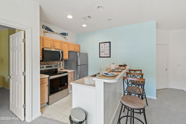 kitchen with decorative backsplash, appliances with stainless steel finishes, light colored carpet, and a kitchen breakfast bar