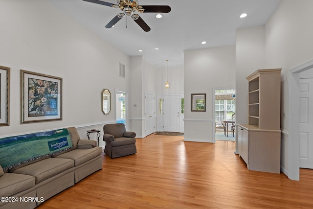 living room with plenty of natural light, ceiling fan, a towering ceiling, and light hardwood / wood-style flooring