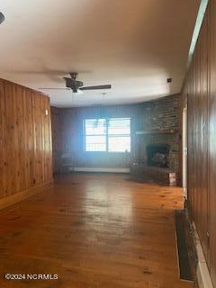 unfurnished living room with wooden walls, hardwood / wood-style flooring, ceiling fan, and a large fireplace