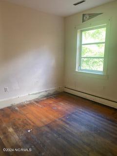 unfurnished room with baseboard heating and dark hardwood / wood-style floors