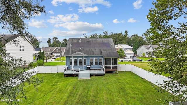 back of property featuring solar panels, a sunroom, a lawn, and a wooden deck