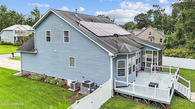 rear view of house with a lawn, a sunroom, solar panels, a deck, and central AC