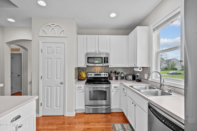 kitchen with appliances with stainless steel finishes, a healthy amount of sunlight, sink, light hardwood / wood-style flooring, and white cabinets